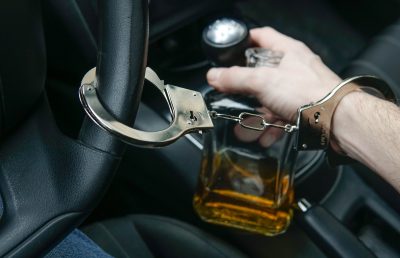 Man in handcuffs holds bottle of alcohol in car. Drunk driving concept. Don’t drink and drive. Man in handcuffs holds bottle of alcohol in car. Drunk driving concept. Don't drink and drive.
