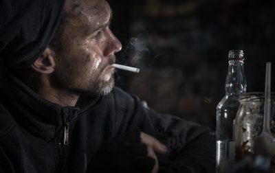 Homeless Men with Cigarette and Bottle of Vodka Dirty Caucasian Homeless Men in His 40s with Cigarette and Bottle of Vodka. Social Issues Theme.